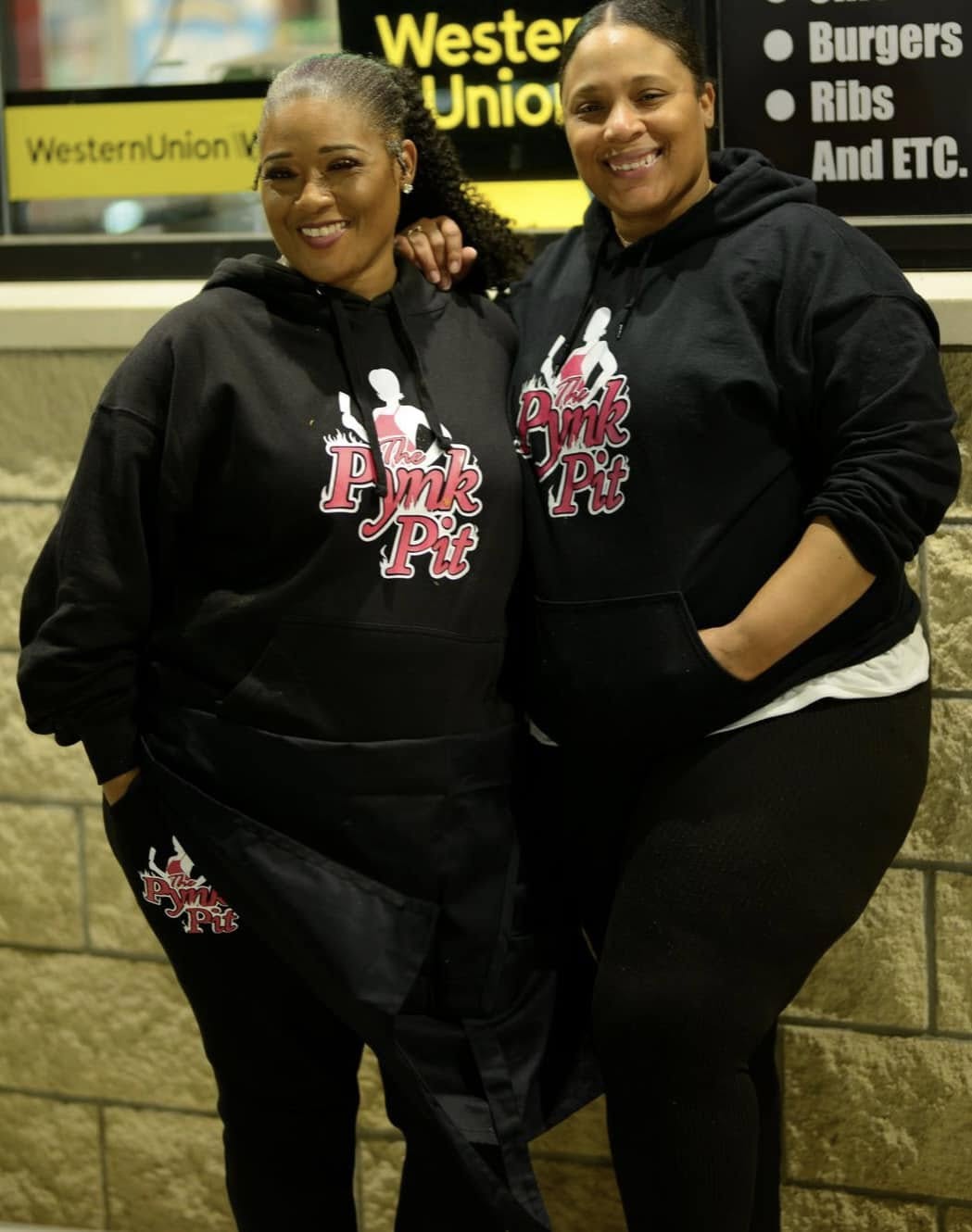 Two PYNK PIT team members wearing branded hoodies